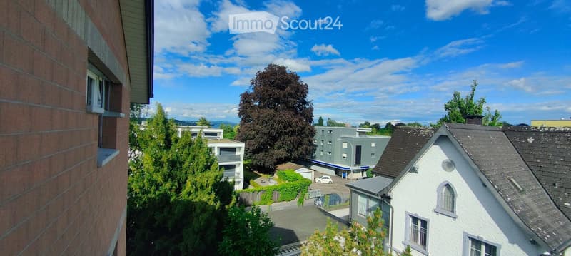 Balcony view overlooking a residential area with trees, buildings, and a clear blue sky.