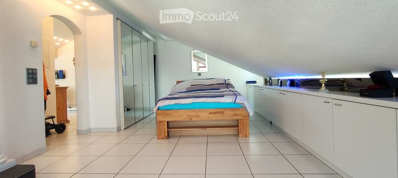 Modern bedroom with a wooden bed, blue and white bedding, white cabinets, a mirror, and a small stool near the entrance.