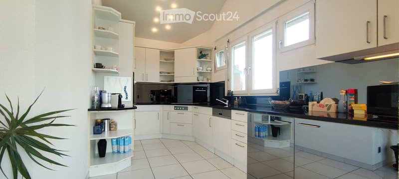 Modern kitchen with white cabinets, black countertops, and stainless steel appliances. Features include a refrigerator, oven, dishwasher, sink, and various kitchen items on the counters and shelves.