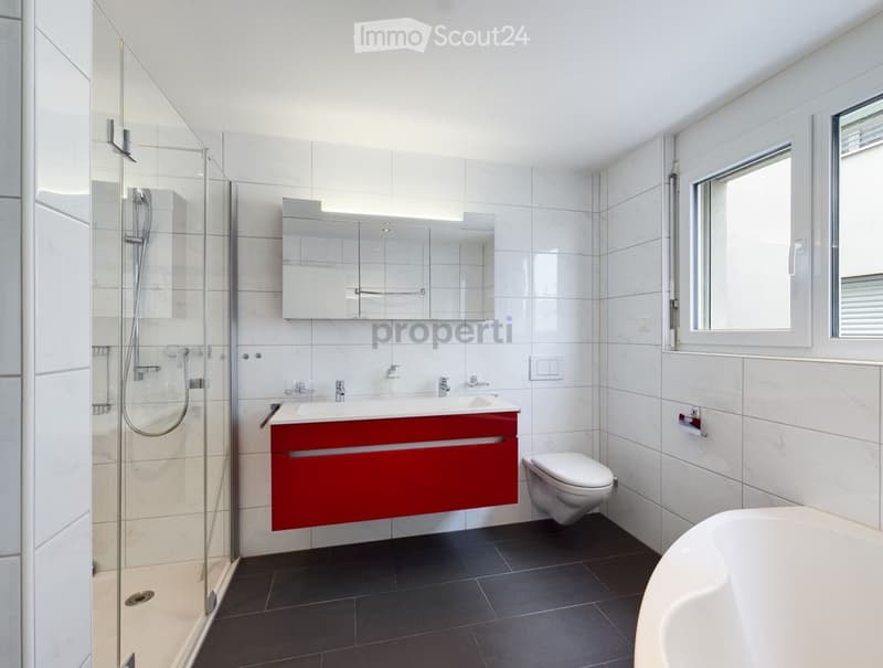 Modern bathroom with white tiles, red vanity, bathtub, toilet, and glass-enclosed shower.