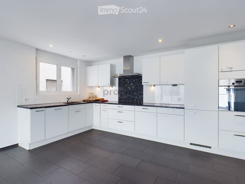 Modern kitchen with white cabinets, dark countertops, and stainless steel appliances. Features a sink, faucet, oven, and range hood.