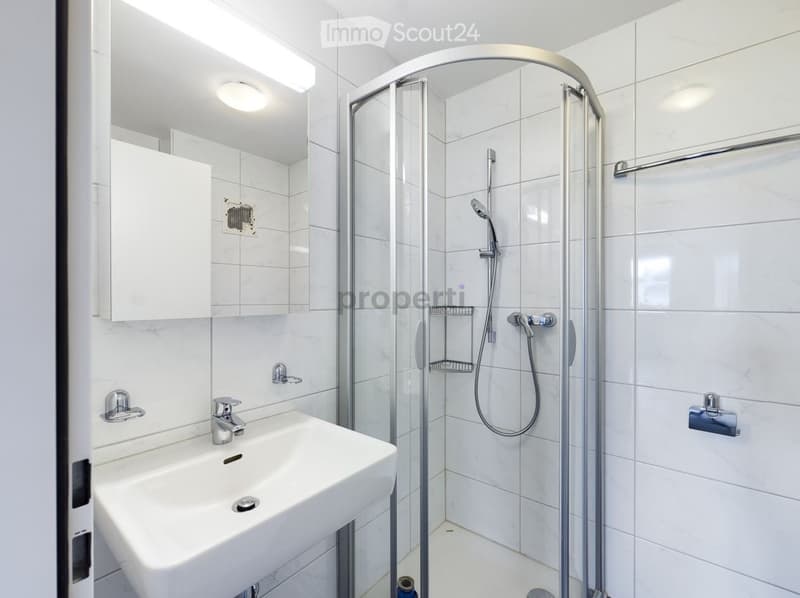 Modern bathroom with white tiles, a glass-enclosed shower, a sink with a mirror, and a built-in cabinet.