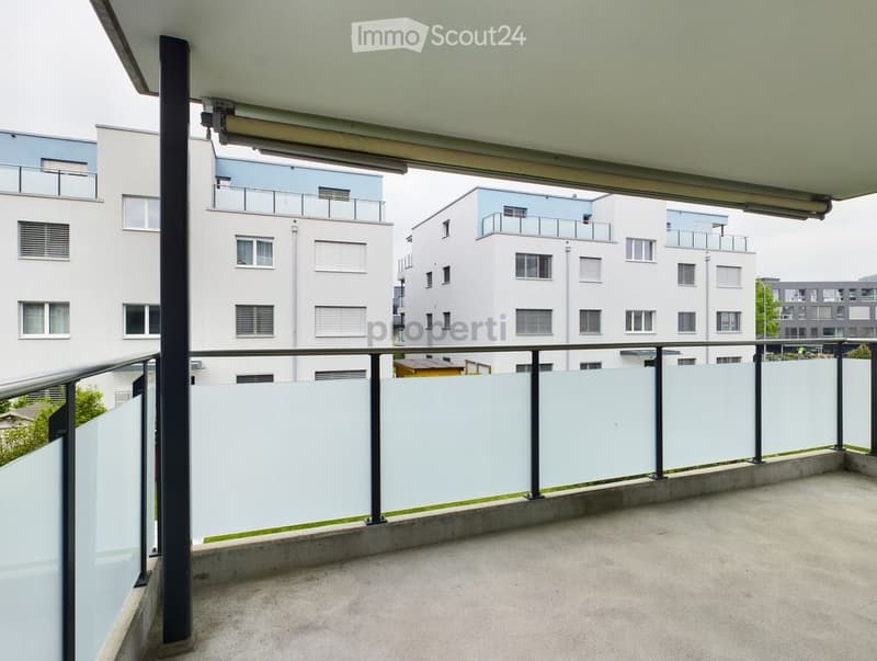 Balcony with modern glass railing, concrete floor, and a view of surrounding buildings.