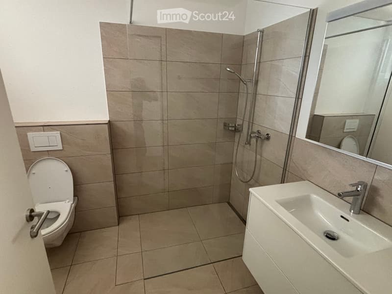 Modern bathroom with beige tiles, a toilet, a sink with a modern faucet, a large mirror, and a shower with a handheld sprayer.