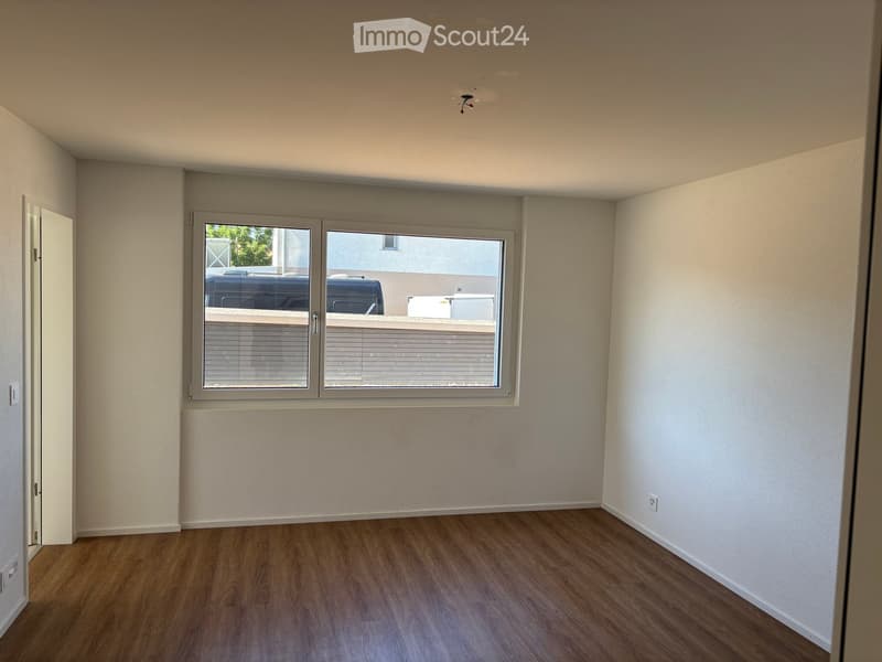 Empty room with wooden flooring, white walls, and a large window with blinds. No furniture or equipment is present.