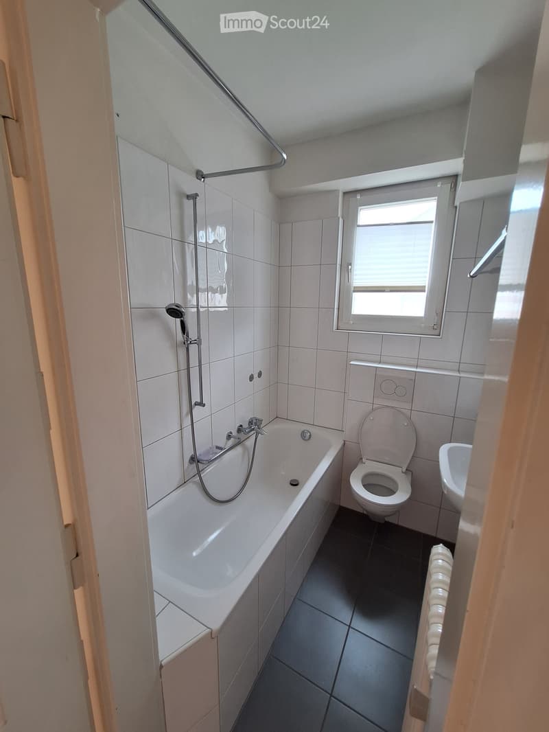 Modern bathroom with white tiles, a bathtub, toilet, sink, and a shower hose attached to the wall.