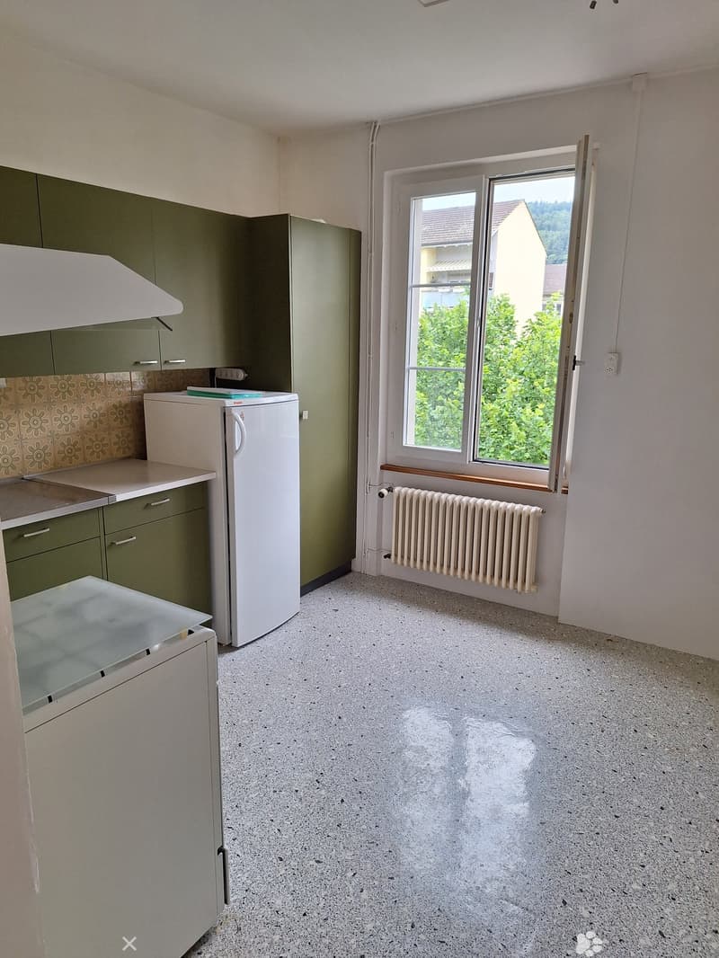 Empty kitchen with green cabinets, a white refrigerator, a sink, and a window overlooking greenery.