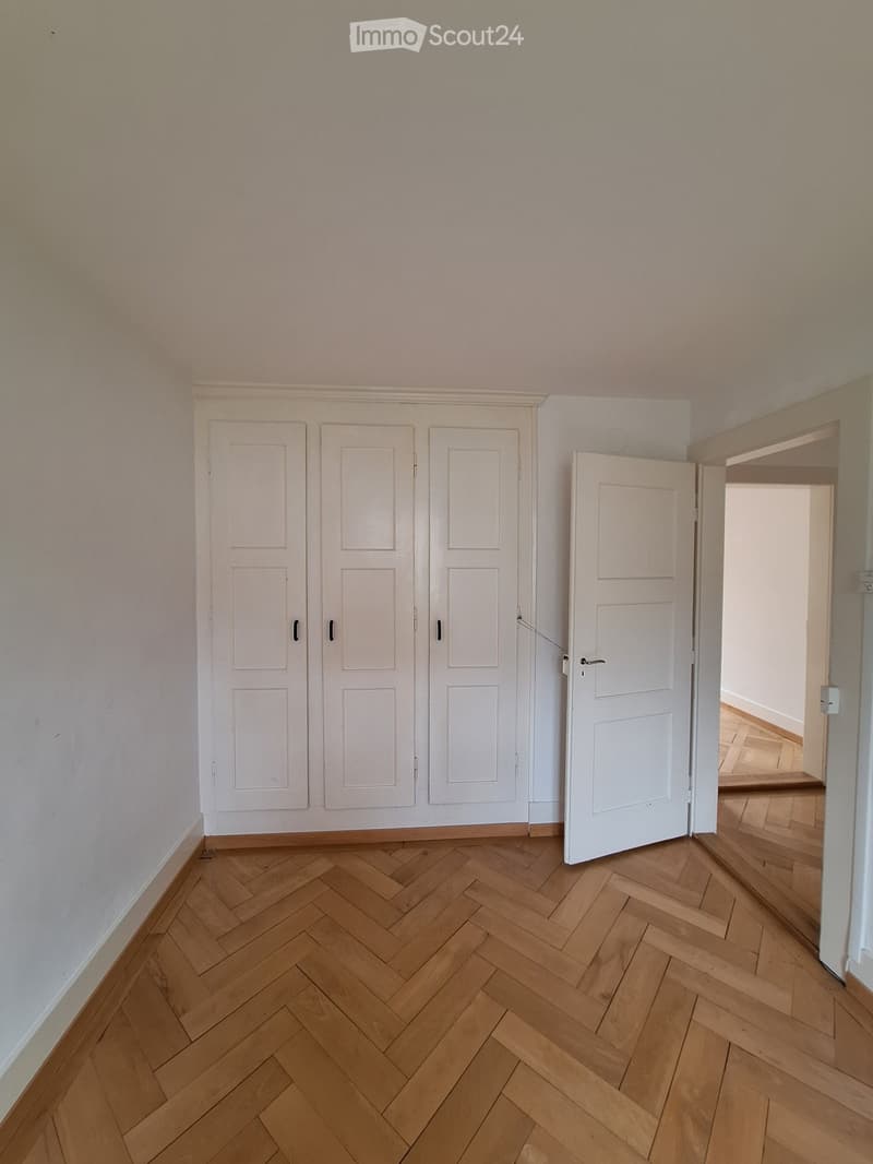 Empty room with wooden herringbone flooring, white walls, and three white doors.