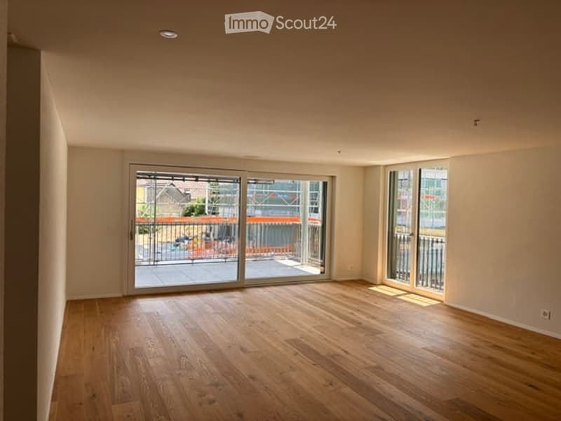 Empty room with wooden flooring, large sliding glass doors leading to a balcony, and white walls.