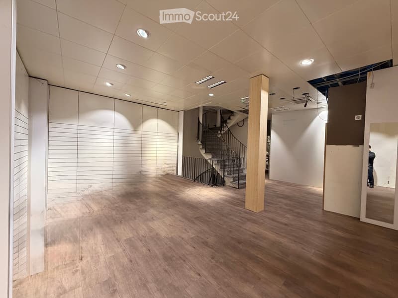 Empty room with wooden flooring, white walls, and a staircase leading to another level. The space is well-lit with recessed ceiling lights.