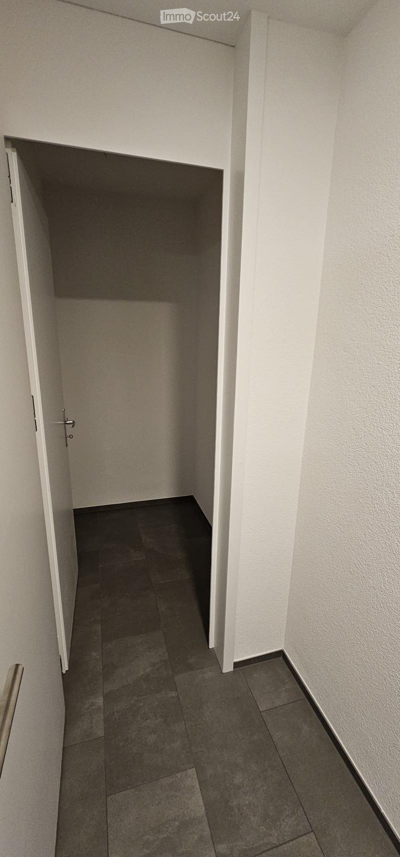 A narrow hallway with tiled flooring and white walls, featuring an open door leading to another room.