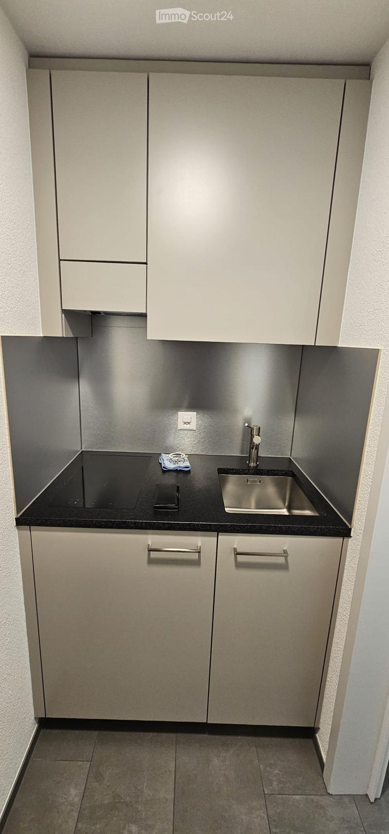Compact kitchen with stainless steel sink, faucet, black countertop, and modern cabinets.