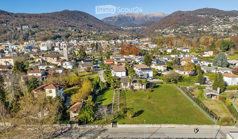 Aerial view of a town nestled in a valley with surrounding mountains, featuring houses, green spaces, and a central lawn area.