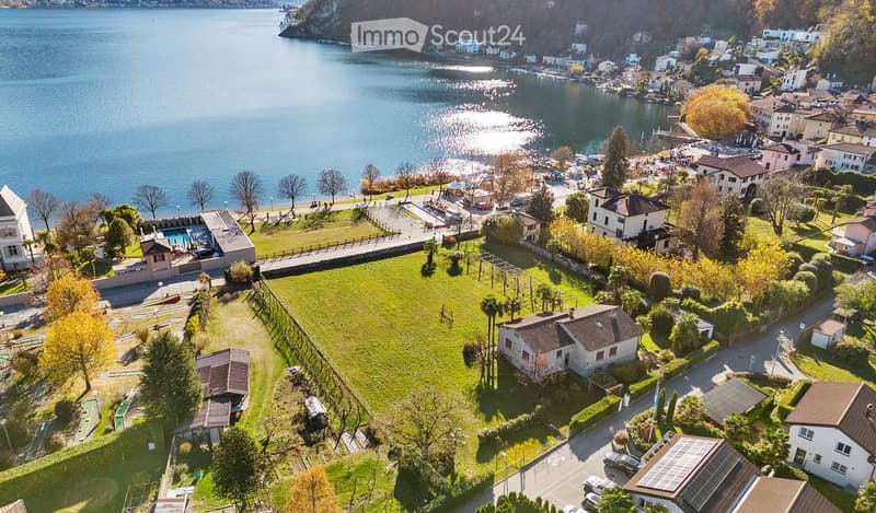Aerial view of a lakeside town with houses, a swimming pool, and a large green lawn area.