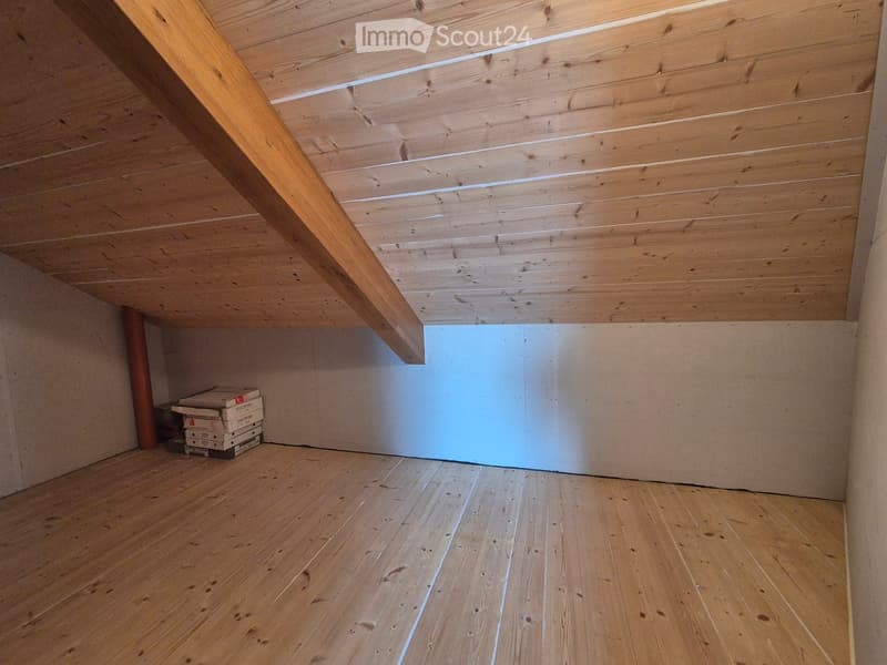 Empty room with wooden floor and exposed wooden ceiling beams. Stack of boxes in the corner.