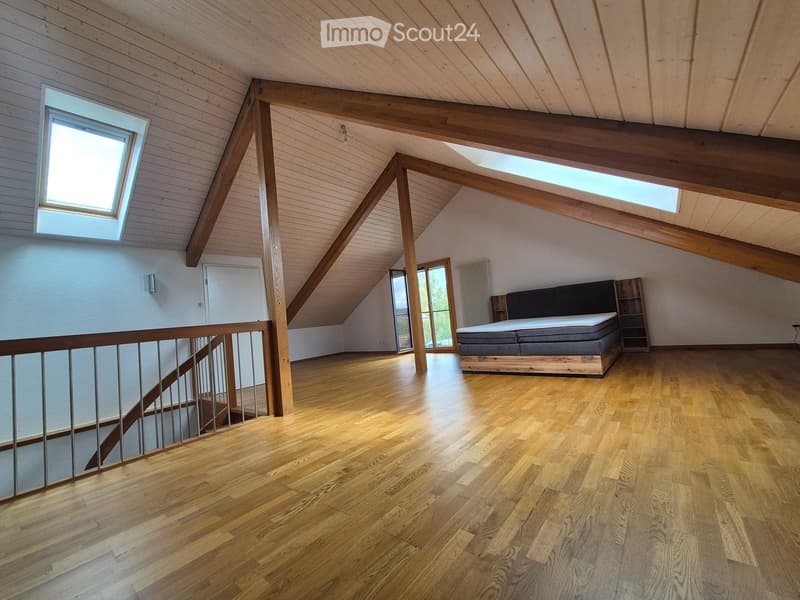 Spacious attic bedroom with wooden floors, exposed wooden beams, skylights, and a modern bed setup.