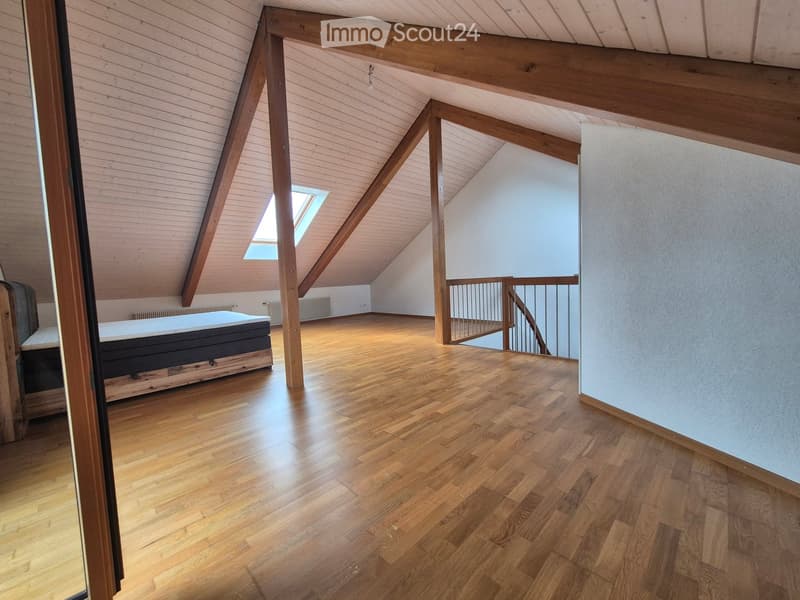 Spacious attic room with wooden floors, exposed wooden beams, skylight window, and a single bed.