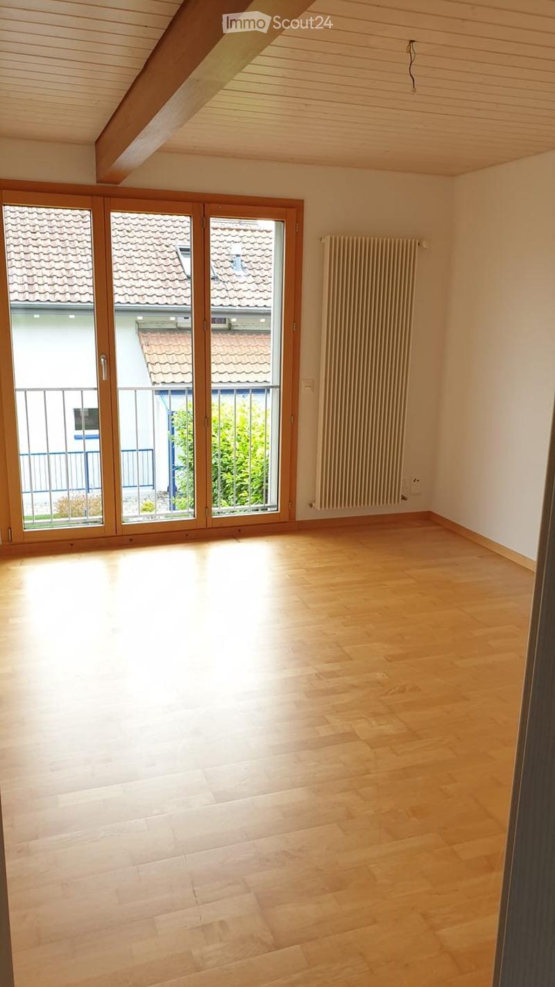 Empty room with wooden flooring, large sliding glass doors leading to a balcony, and a radiator on the wall.