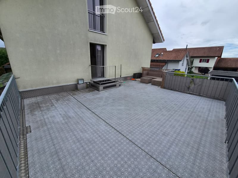 Balcony with grey tiled floor, metal railing, and access to a room with a window and sliding door.