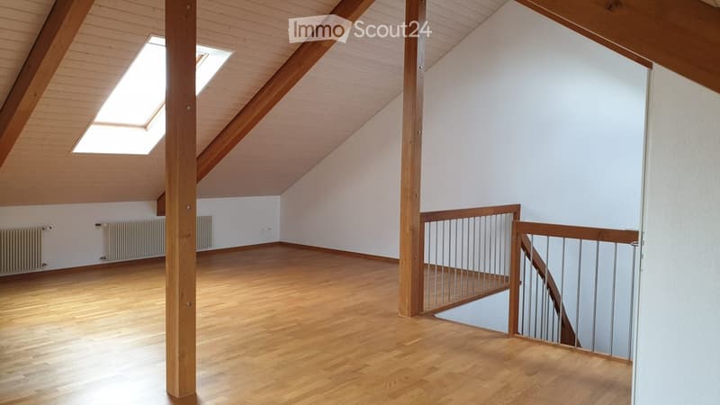 Empty attic space with wooden floors, white walls, exposed wooden beams, and a metal staircase leading downwards.
