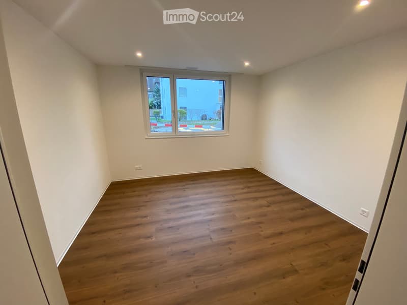 Empty room with wooden flooring, white walls, and a large window with a view of the outside.