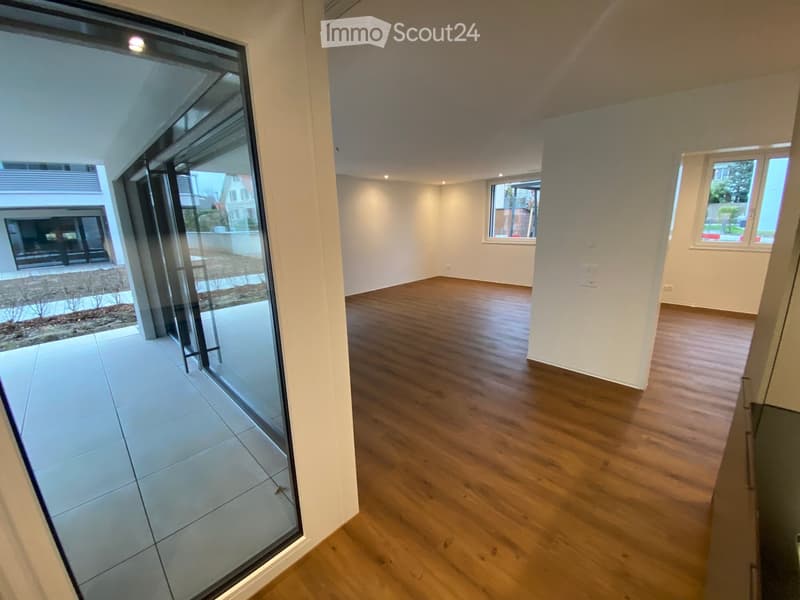 Empty room with wooden flooring, white walls, large windows, and a glass door leading to a tiled outdoor area.