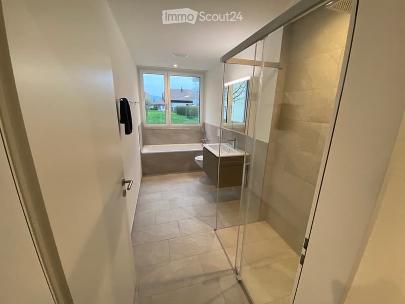 Modern bathroom with a bathtub, toilet, sink, and a glass-enclosed shower area. The space features tiled floors and walls, with a window providing natural light.