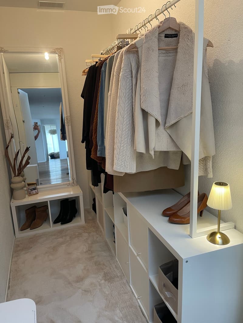 Well-organized walk-in closet with a large mirror, wardrobe, shelves, and storage compartments. Features include a lamp, decorative vase, and neatly arranged shoes and clothing.