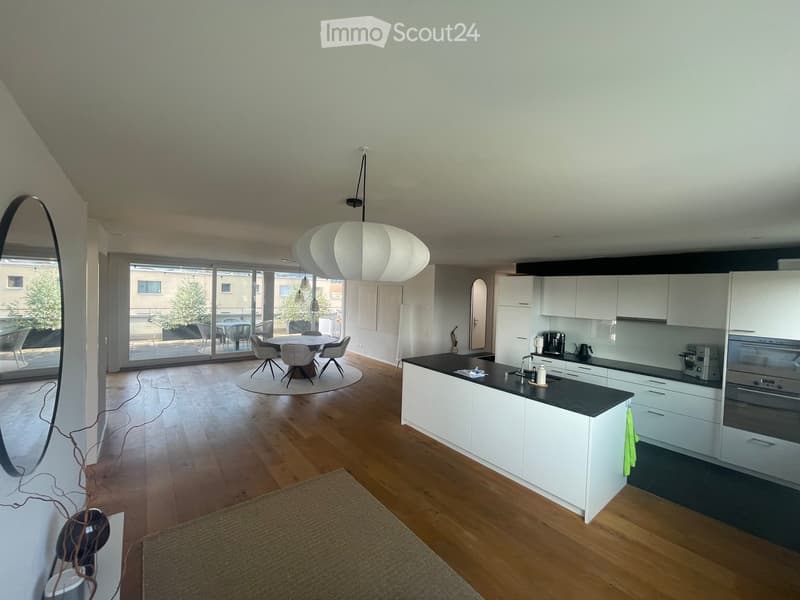 Modern kitchen with white cabinets, black countertop, and wooden flooring. Features a kitchen island, sink, oven, coffee maker, and a dining area with a table and chairs.