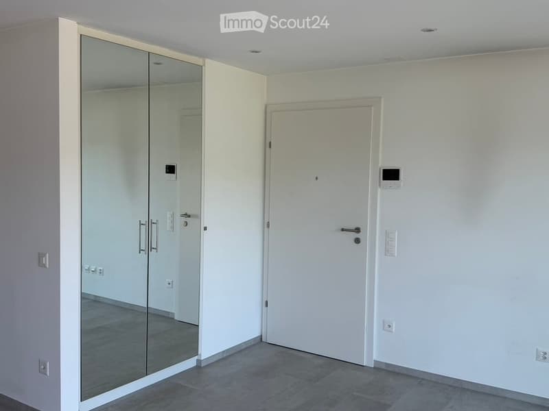 Empty room with white walls, grey tiled floor, mirrored closet with silver handles, and a white door with a silver handle.