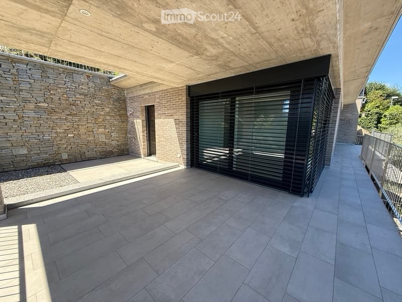 Modern balcony with concrete ceiling, tiled floor, stone wall, and large sliding glass door.