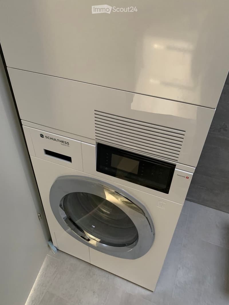 Modern white washing machine with digital display and control panel, placed on tiled floor.