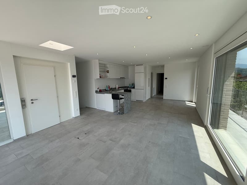 Modern, open-plan living and dining area with a kitchen, white cabinets, a refrigerator, a bar stool, and a large window offering a view.