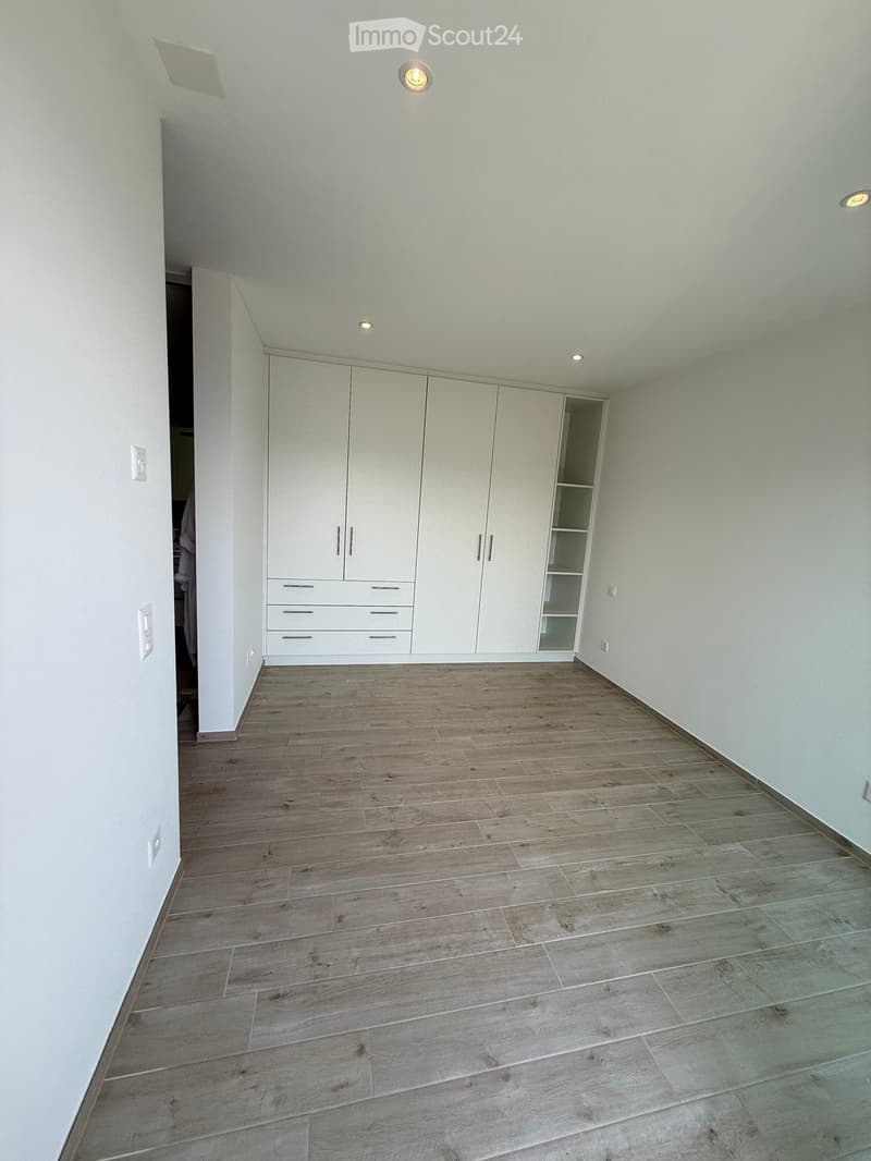 Empty room with white walls, wooden flooring, and built-in white cabinetry with drawers and shelves.
