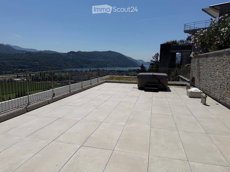 Spacious balcony with tiled floor, metal railing, and scenic mountain view. Includes a covered seating area and a small table.