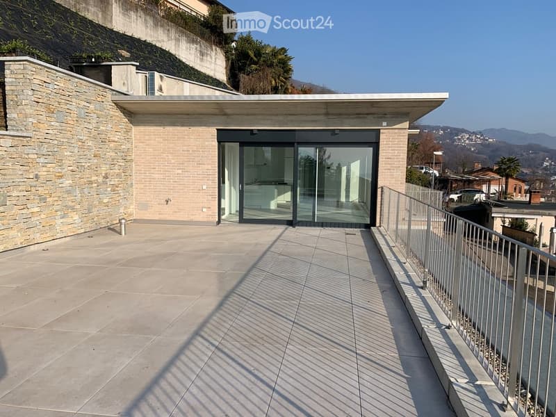 Modern outdoor patio with large sliding glass doors leading to a house, stone walls, and a scenic view of the surrounding landscape.