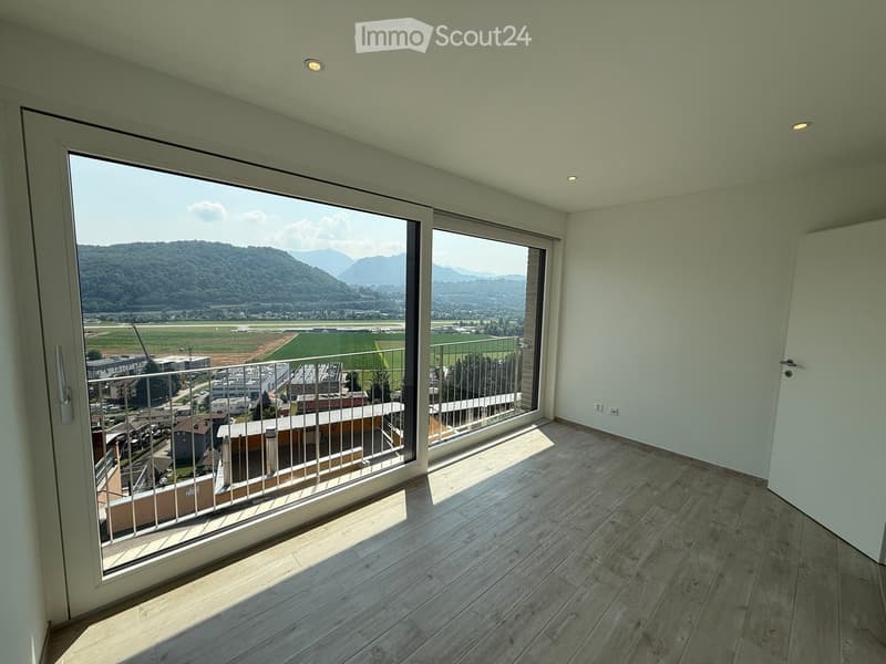Empty balcony with wooden flooring, large glass doors, metal railing, and scenic mountain view.
