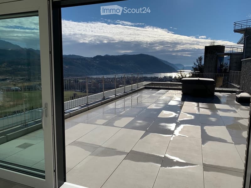 Modern balcony with large glass doors, tiled floor, metal railing, and scenic mountain and lake view.