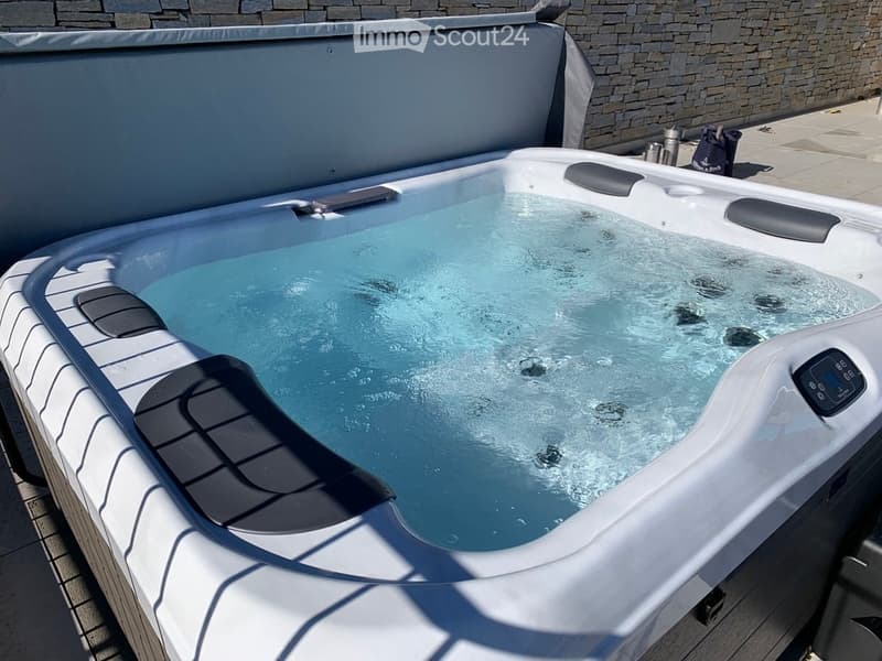 Modern hot tub with clear water, black seating, and control panel, situated on a wooden deck next to a stone wall.