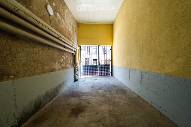 Empty hallway with concrete floor, yellow walls, and a metal gate at the end.