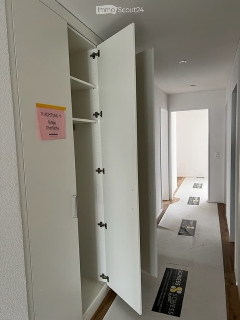 Empty hallway with white walls, wooden flooring, and an open closet with empty shelves.