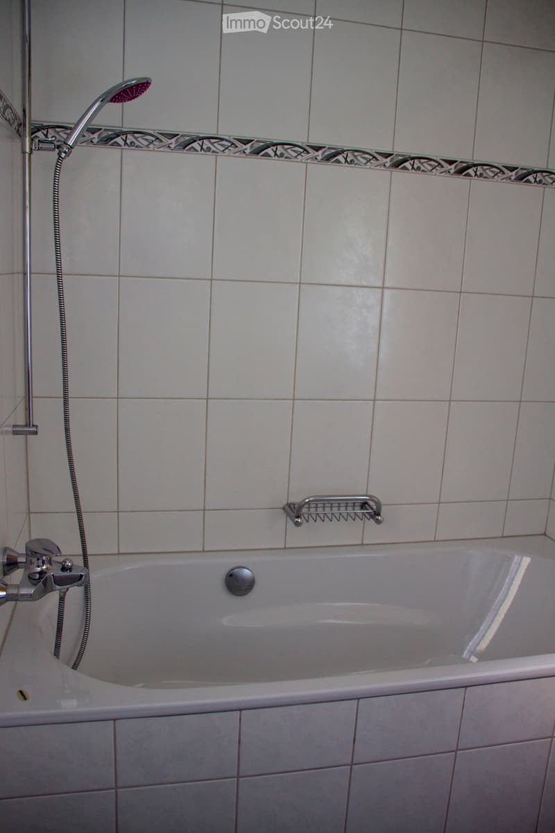 Bathtub with a modern faucet and a handheld showerhead, accompanied by a towel rack on the wall.