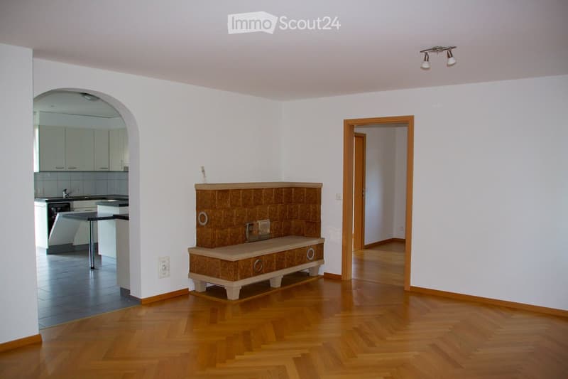 Bright living room with wooden flooring, a decorative bench, a small table, and an open kitchen area with white cabinets, a sink, and an oven.