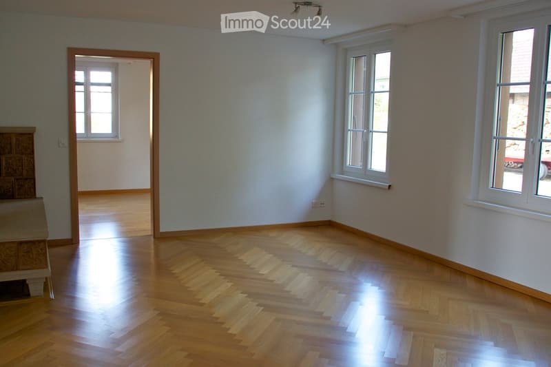 Empty room with wooden flooring, white walls, and multiple windows allowing natural light. The room is unfurnished with no visible furniture or equipment.