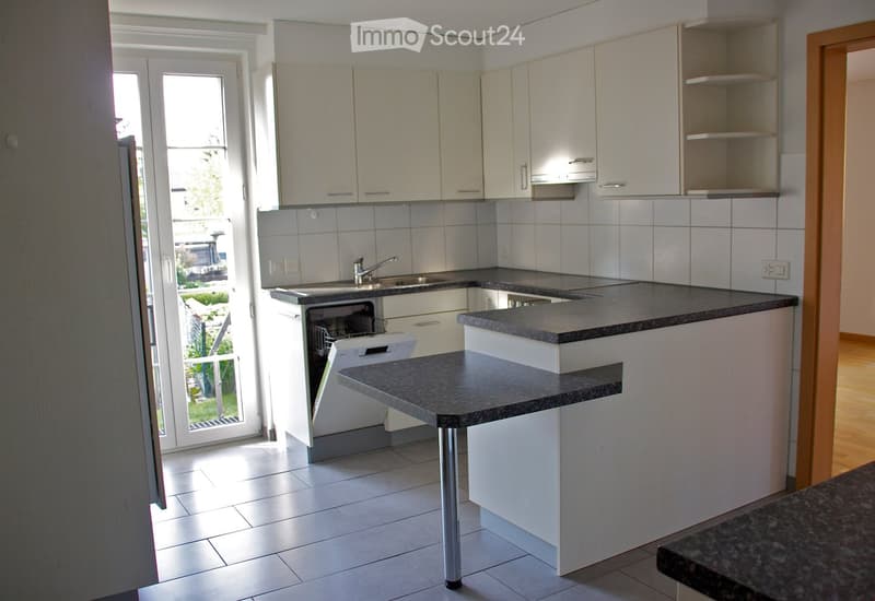 Modern kitchen with white cabinets, granite countertops, a dishwasher, and a sink. The space is bright with natural light from a large window and door leading to an outdoor area.