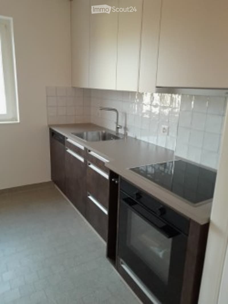 Modern kitchen with white cabinets, stainless steel sink and faucet, built-in oven and stove, tiled backsplash, and light-colored countertops.