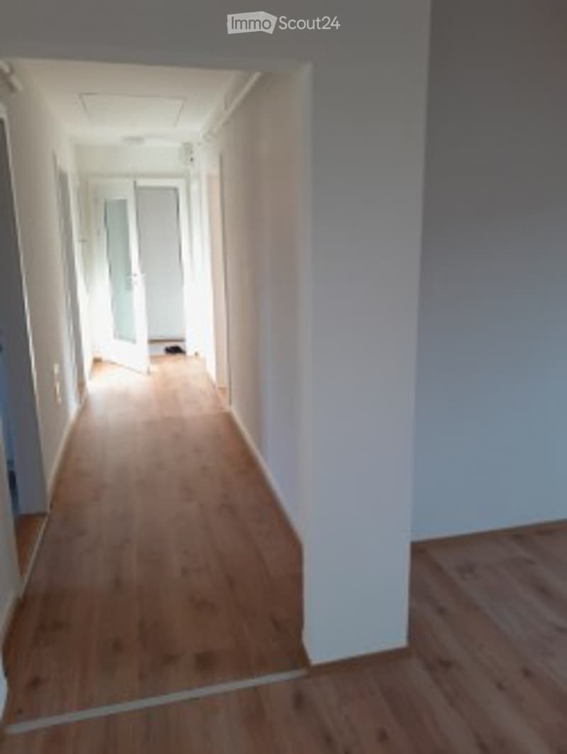 Empty hallway with light wooden flooring and white walls, leading to a door at the end.