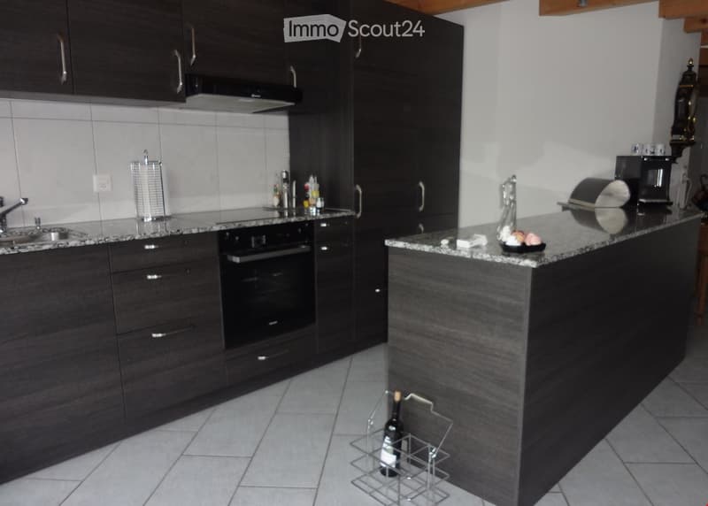 Modern kitchen with dark wood cabinets, granite countertops, stainless steel appliances, and a bottle rack on the floor.