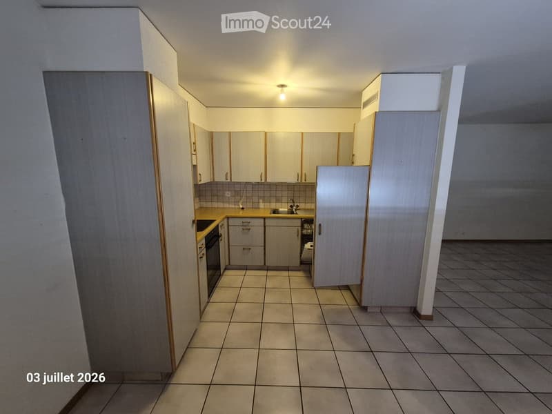 Empty kitchen with light-colored cabinets, tiled floor, and basic appliances like a sink and stove, but no furniture or personal items.