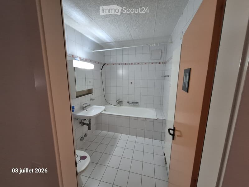 Clean, tiled bathroom with a white sink, bathtub, mirror, and toilet. The walls are tiled with a decorative border, and the floor is covered in white tiles.
